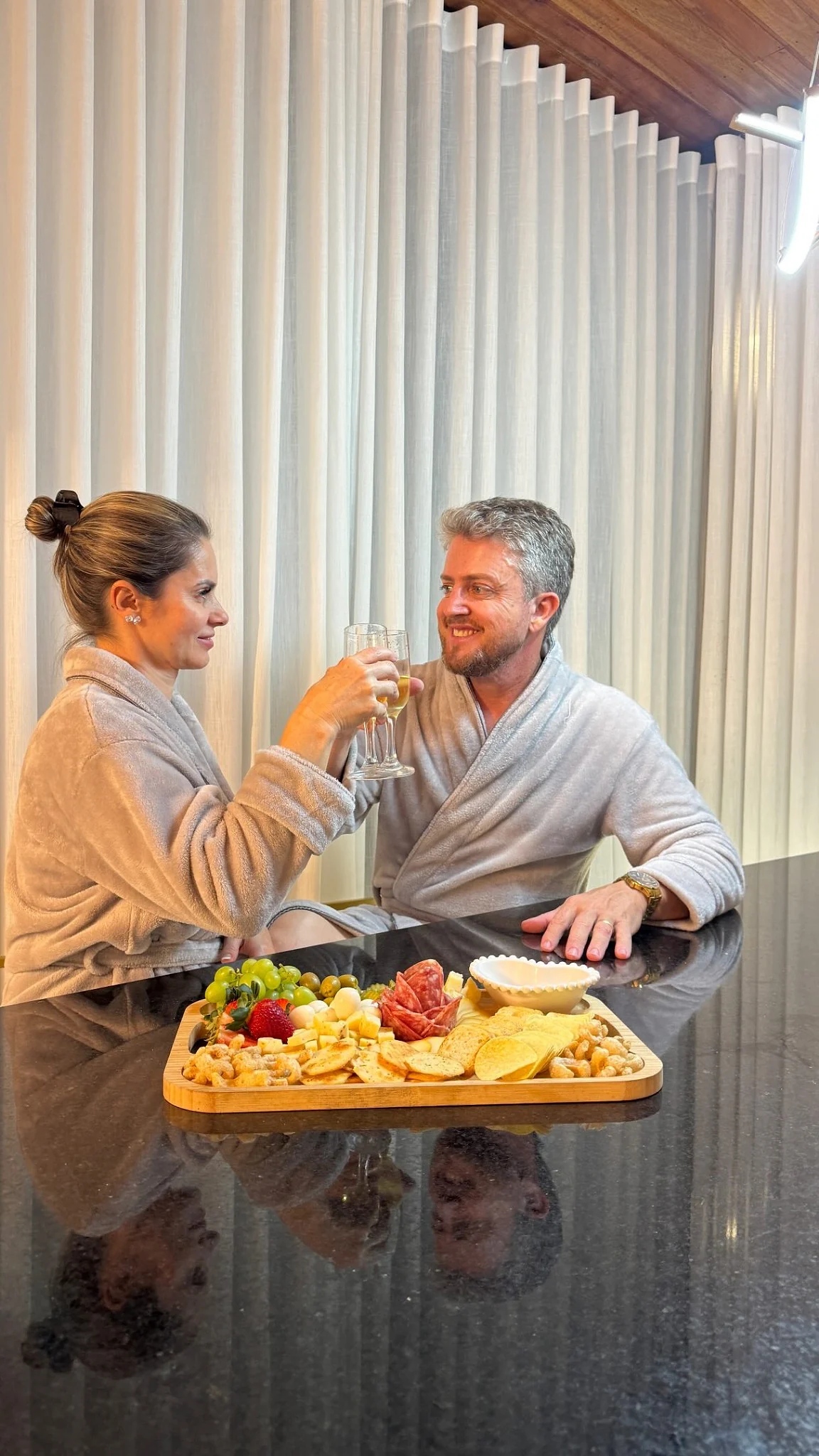 Casal brindando diante de uma tábua de frios na cabana