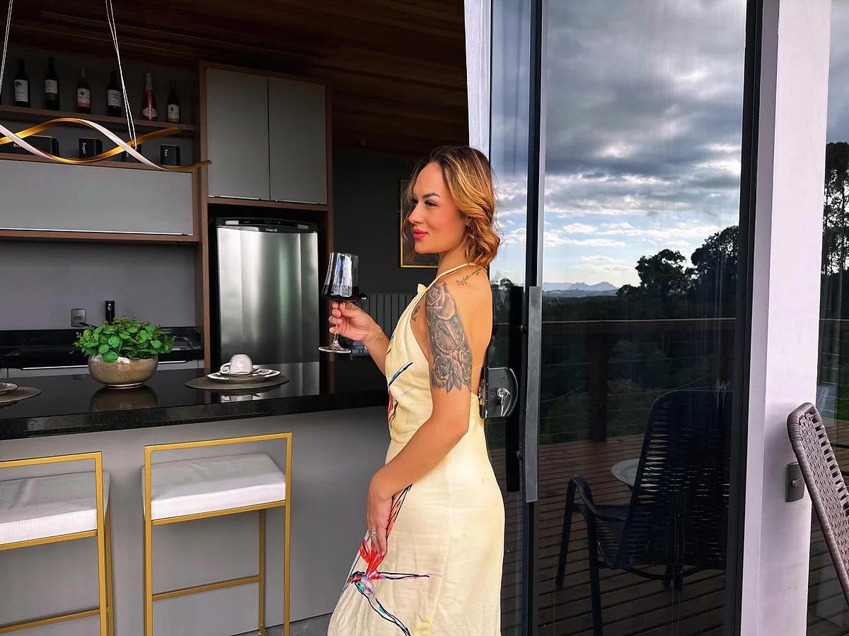 Hóspede com taça de vinho na cozinha integrada da cabana